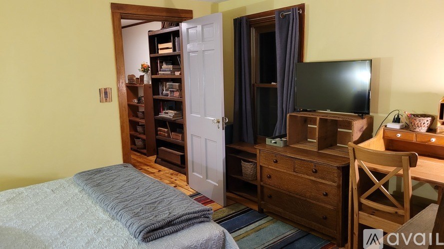 A bedroom with a bed, a dresser with a television on top, and a chair.