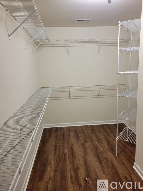 Empty walk-in closet with wooden floors and white shelving.