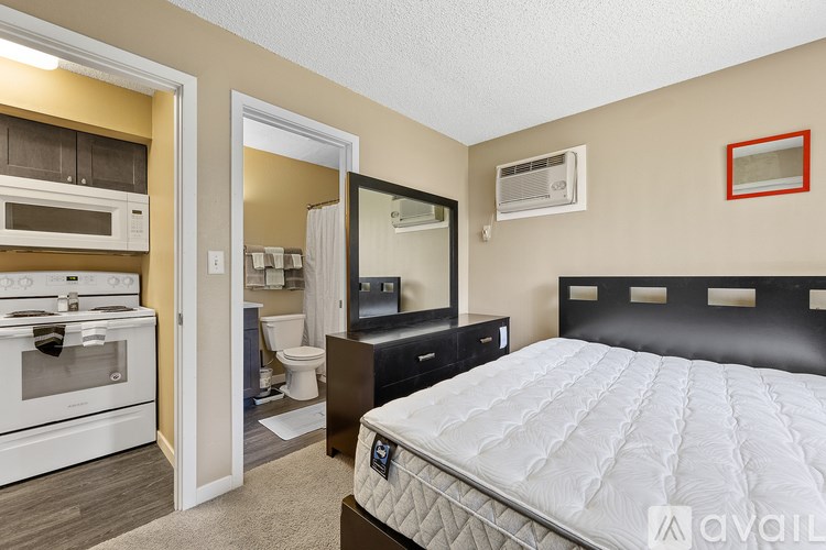 A bedroom with a large bed, a kitchen area with a stove, and a bathroom with a toilet and sink.