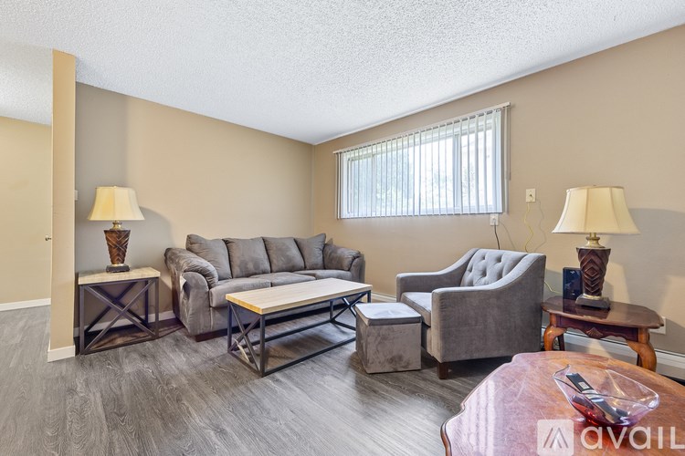 A living room with a grey couch, a grey armchair, a grey chair, a grey ottoman, a wooden coffee table, and two lamps.