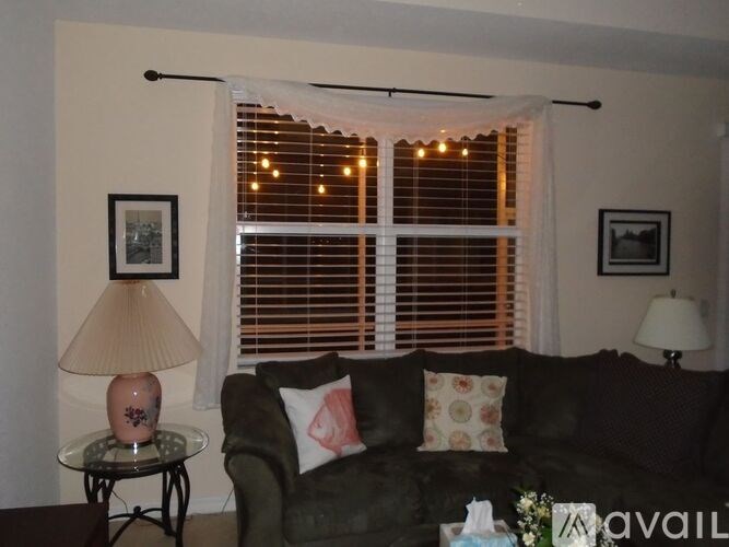 A living room with a black couch, a table with a lamp, and a window with blinds.