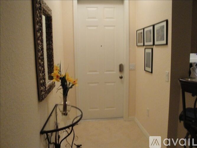 A hallway with a white door, a table with flowers, and pictures on the wall.