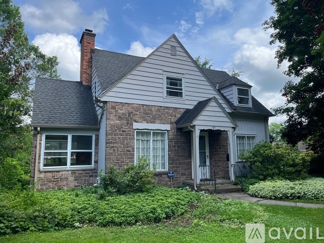 A house with a grey roof and a brick chimney is surrounded by greenery.