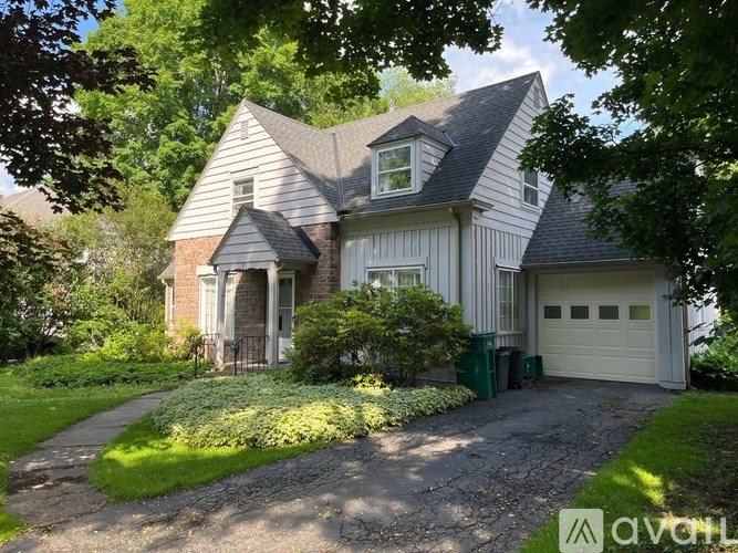 A house with a grey roof and white walls is surrounded by greenery.