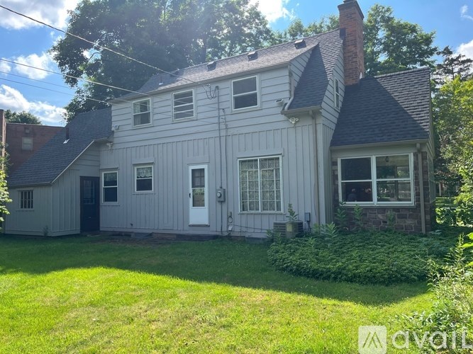 A house with a grey exterior and a white door is surrounded by greenery.