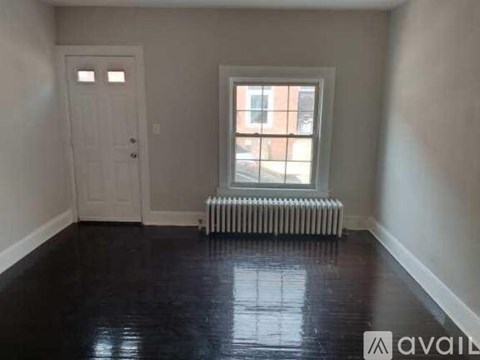 A room with a white door and a window with a white radiator beneath it.