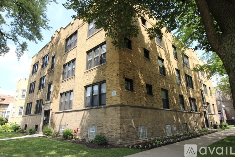 A tall brick building with many windows is surrounded by trees.