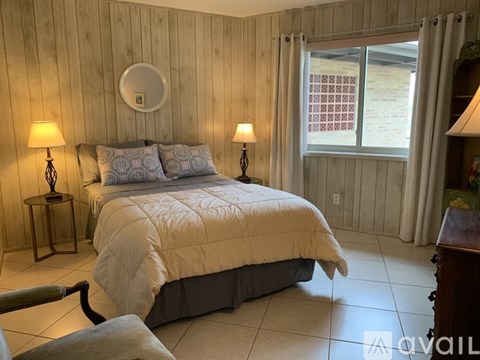 A bedroom with a bed, two lamps, and a window with curtains.
