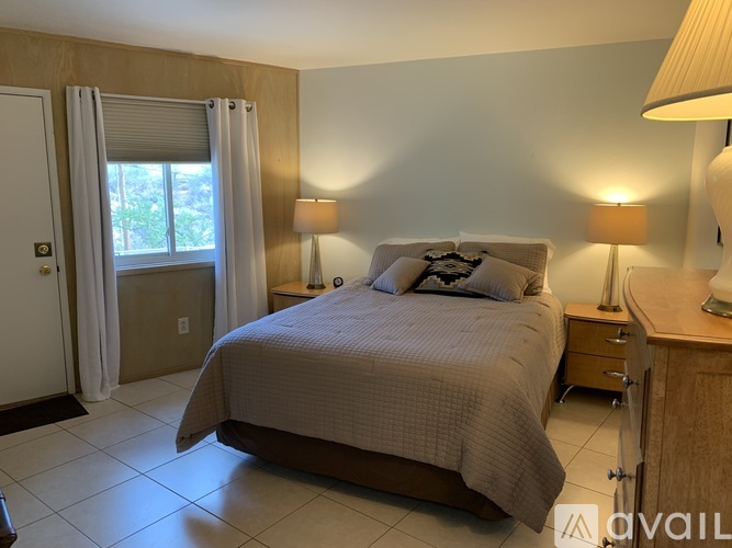 A bedroom with a bed, two lamps, and a window with curtains.