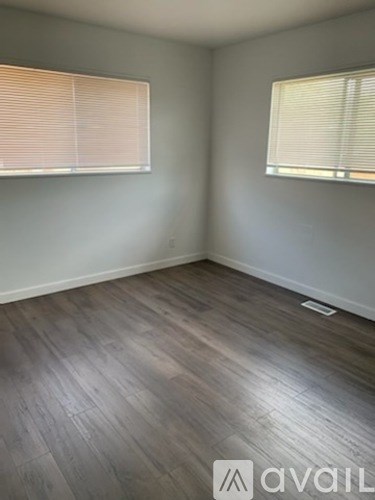 A room with wooden flooring and two windows with blinds.