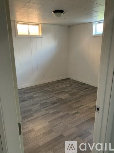 A room with wooden flooring and two windows.