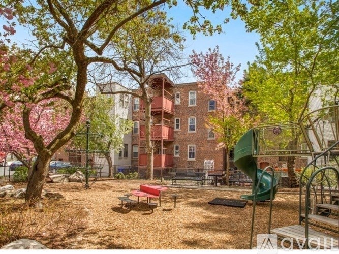 A playground with a red bench and a green slide in front of a red brick building.