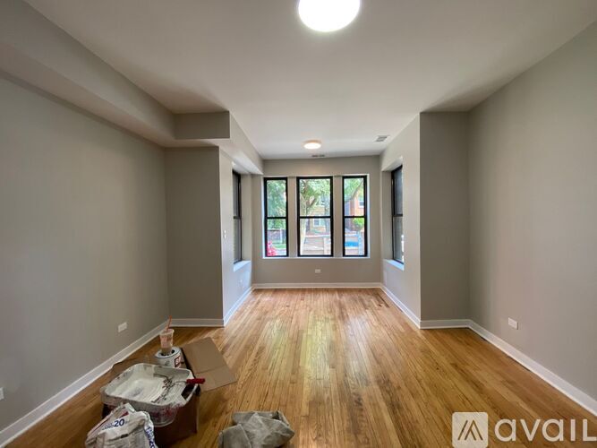 A room with wooden floors and a large window with a view of trees and a building outside.