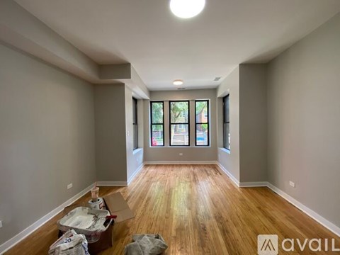 A room with wooden floors and a large window with a view of trees and a building outside.