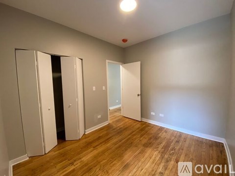 A room with wooden floors and white walls, with a door on the left and a window on the right.