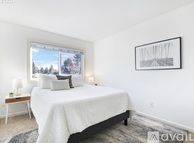 A bedroom with a large bed, a window with a view of trees, and a framed picture on the wall.
