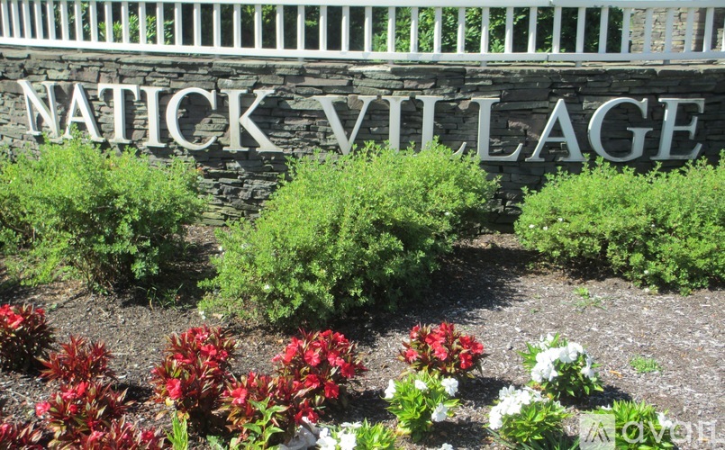 A sign that says Natick Village in front of some bushes.
