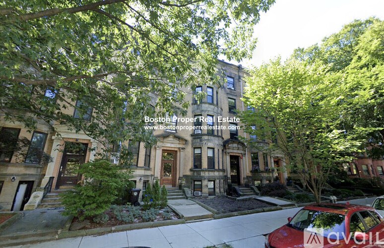 A red car is parked on the street in front of a row of townhouses.