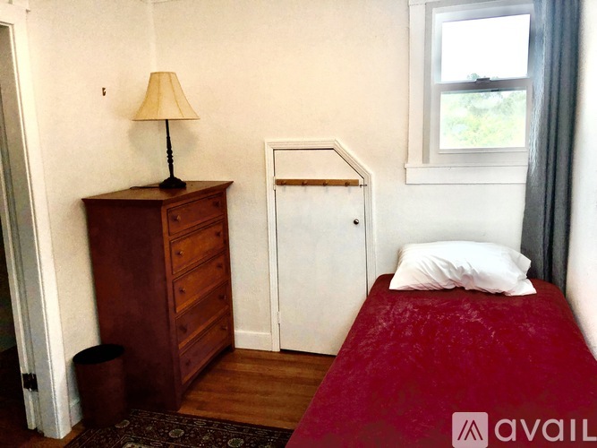 A bedroom with a red bedspread and a wooden dresser with a lamp on it.