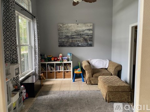 A living room with a chair, ottoman, and a painting on the wall.
