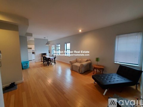 A living room with a black leather couch and wooden floors.