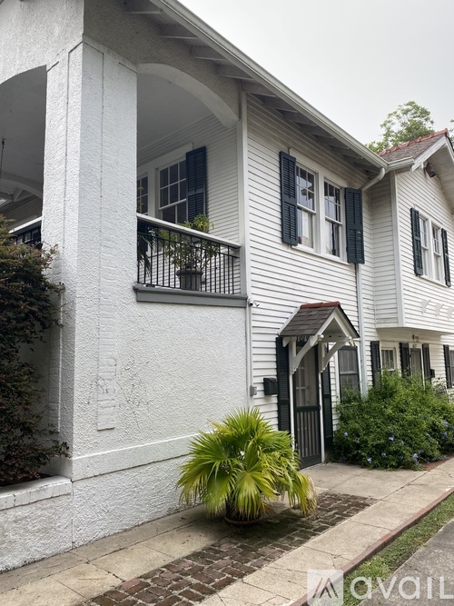 A white house with a balcony and a small garden in front.