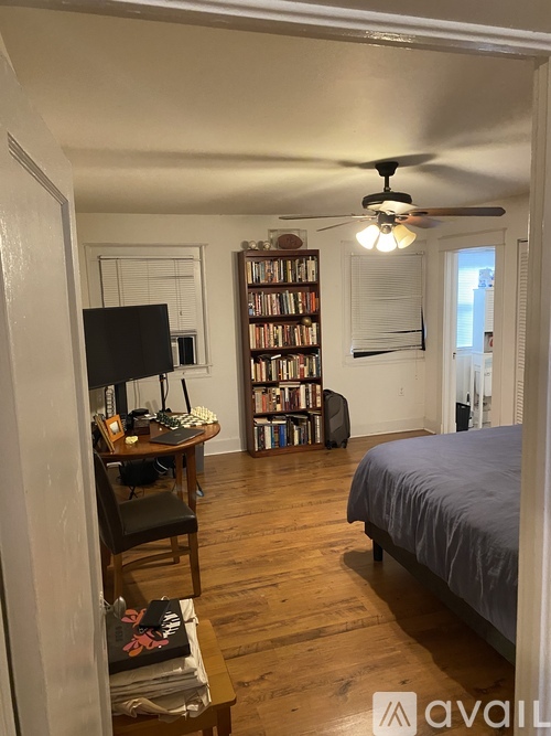 A bedroom with a bed, a chair, a table with a television and a bookshelf.