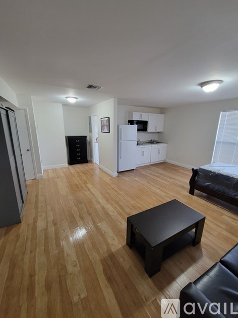 A living room with a black leather couch and a wooden floor.