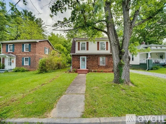 A red brick house with a white door and a tree in front.