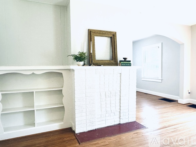 A white fireplace with a gold frame picture on top of it.