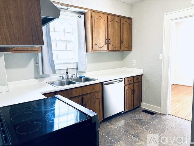 A kitchen with a black stove top oven, wooden cabinets, and a white counter top.