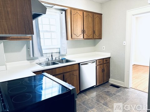 A kitchen with a black stove top oven, wooden cabinets, and a white counter top.