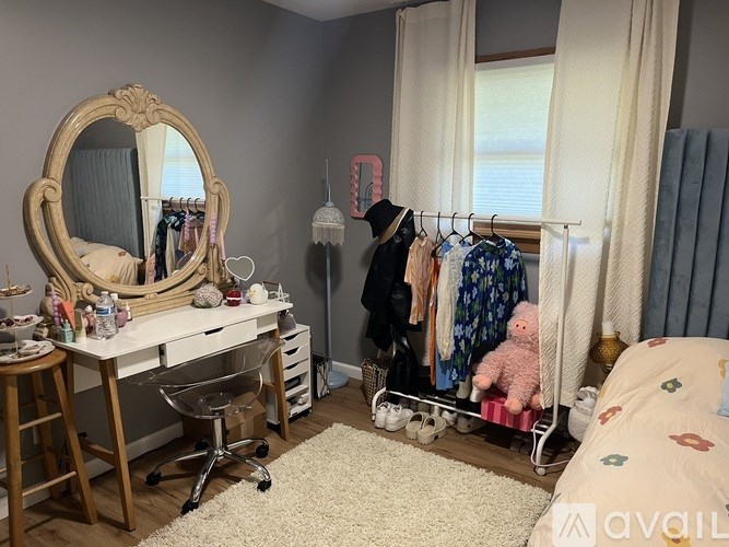 A bedroom with a white desk, a mirror, a chair, a wardrobe, and a bed with a floral pattern.