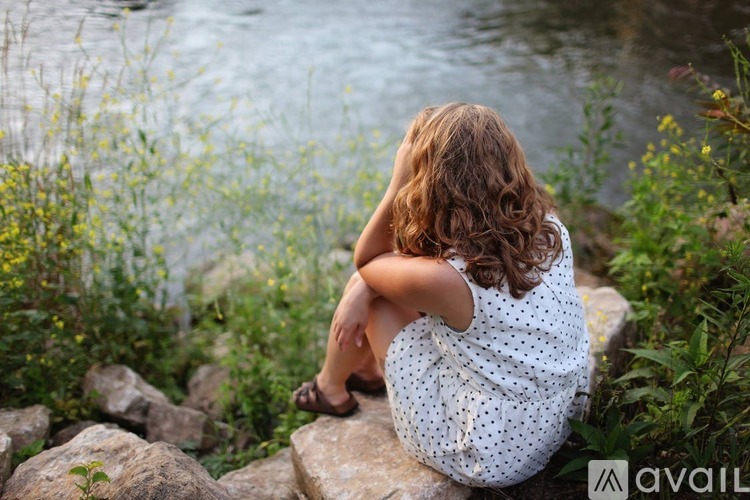 A woman in a white dress sits on rocks by a body of water.