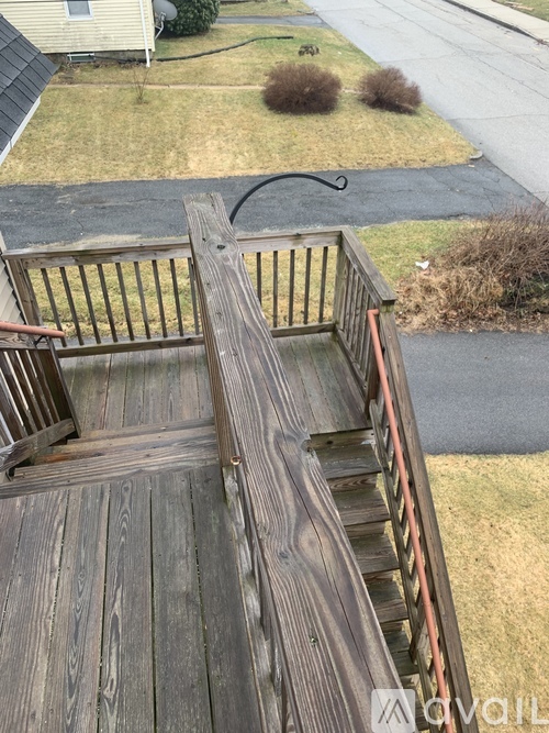 A wooden deck with a railing and steps leading down to a road.