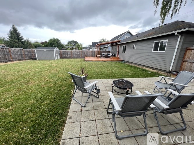 A backyard with a patio, lawn, and a couple of chairs.