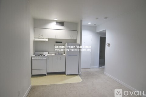 A kitchen area with white appliances and cabinets in a room with a carpeted floor.