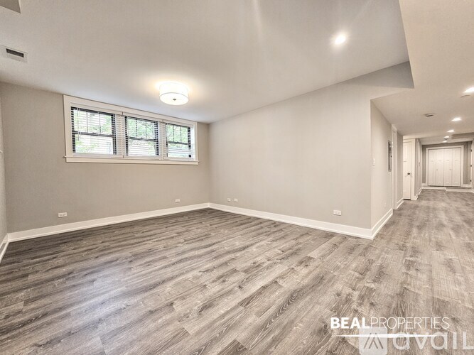 A spacious room with wooden flooring and a window with blinds.