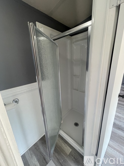 A white shower stall with a glass door is in a bathroom with grey walls.
