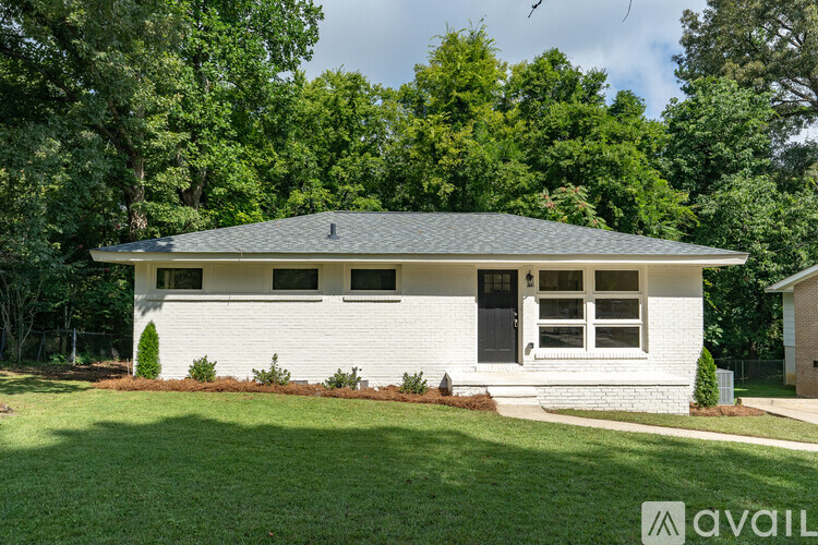 A house with a grey roof and white walls is surrounded by greenery.
