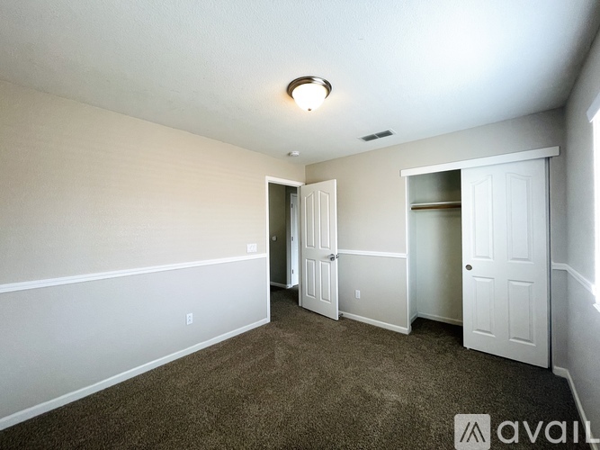 A room with carpeted floor and white walls, with a ceiling light and two doors.