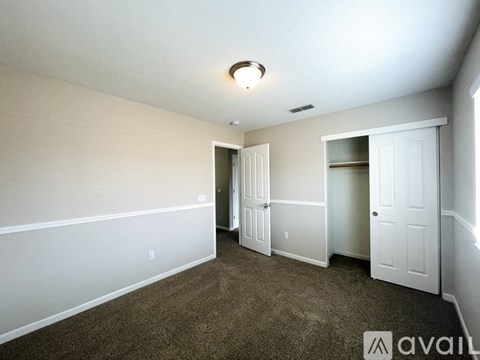 A room with carpeted floor and white walls, with a ceiling light and two doors.