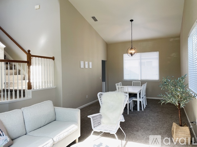 A living room with a white couch, a dining table with chairs, a potted plant, and a hanging light fixture.