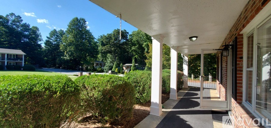 A porch with white columns and a green hedge in front.