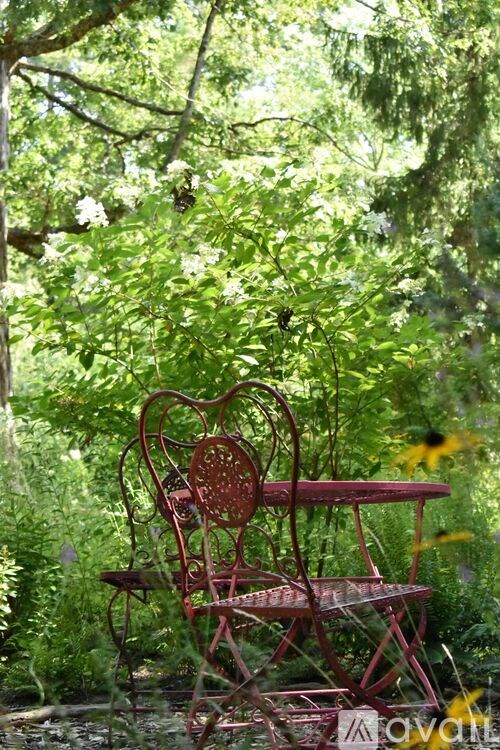 A red metal chair and table are surrounded by greenery.