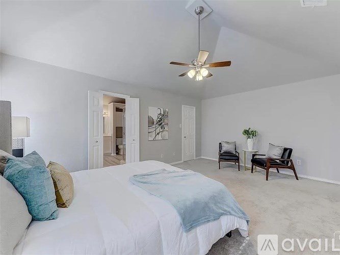 A bedroom with a bed, two chairs, and a ceiling fan.