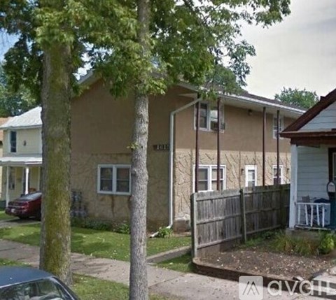 A house with a brown siding and white trim is surrounded by a wooden fence.