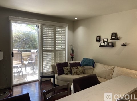 A living room with a white couch, a dining table, and a sliding glass door leading to a patio.