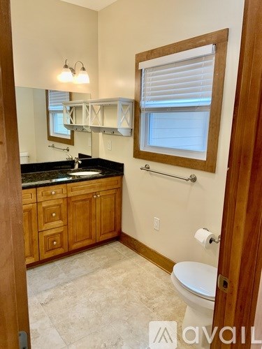 A bathroom with a toilet, sink, mirror, and wooden cabinets.