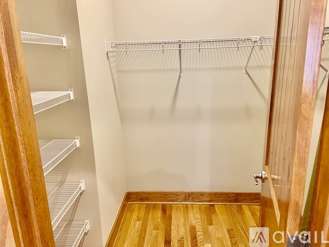 A walk-in closet with wooden floors and white shelving.